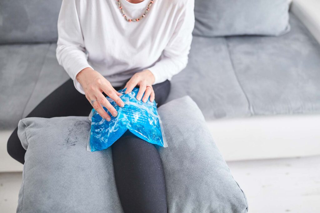 person with ice pack over their knee. the knee is in a raised position on a cushion.