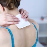 lady putting cold pad on her upper back at base of neck