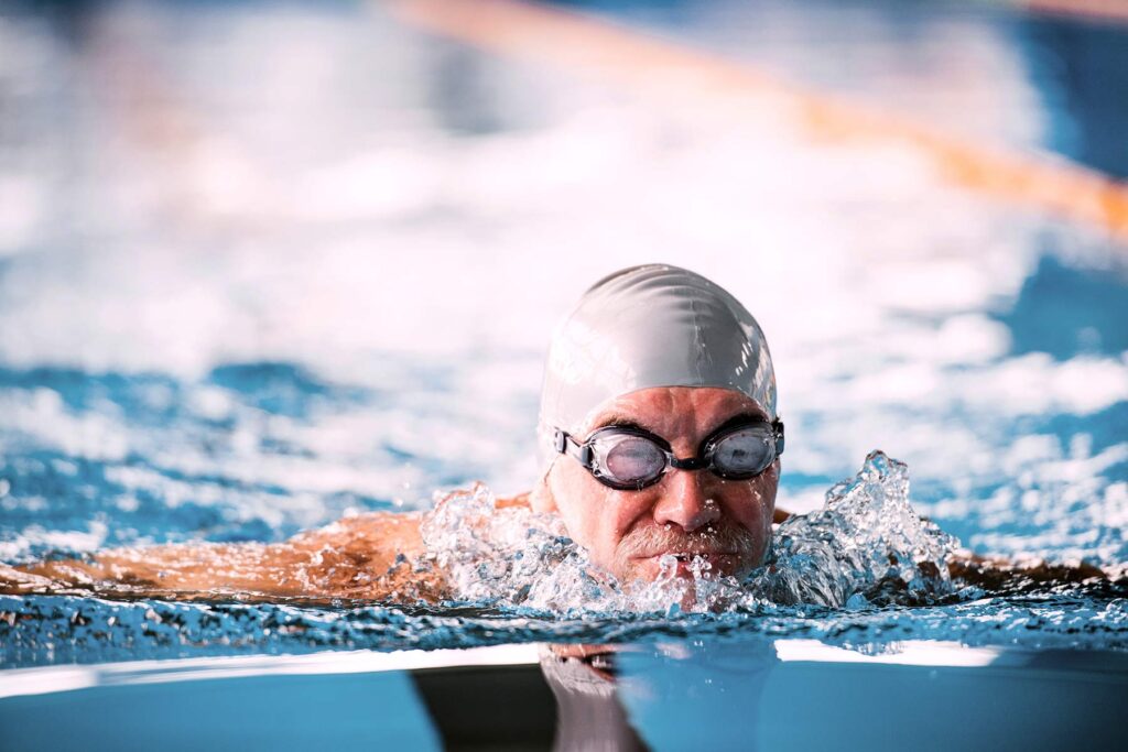 man in grey swimming cap and goggles swimming in a pool