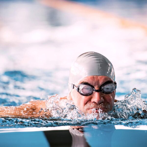 man in grey swimming cap and goggles swimming in a pool