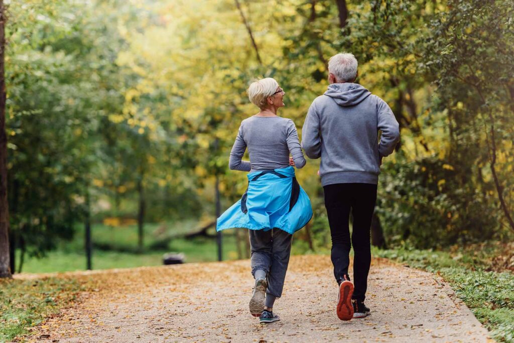 and older man and lady jogging along a path in the autumn