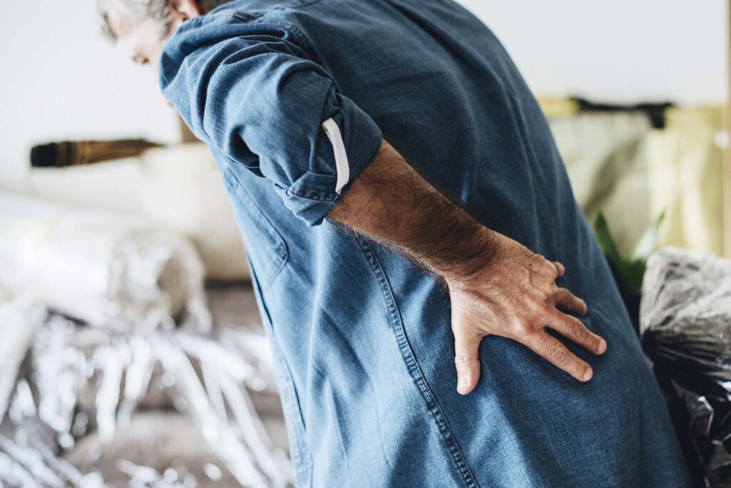 man in blue denim shirt leaning forward clasping his lower back